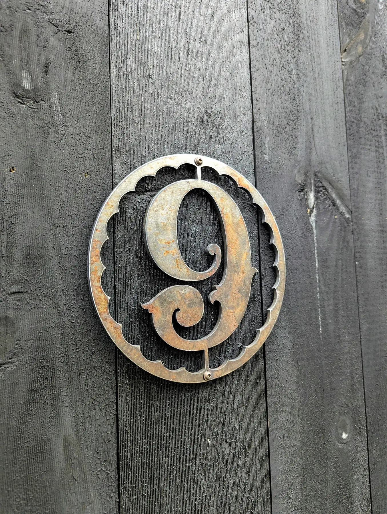 Finished plasma cut metal number nine sign mounted to a dark wood exterior wall
