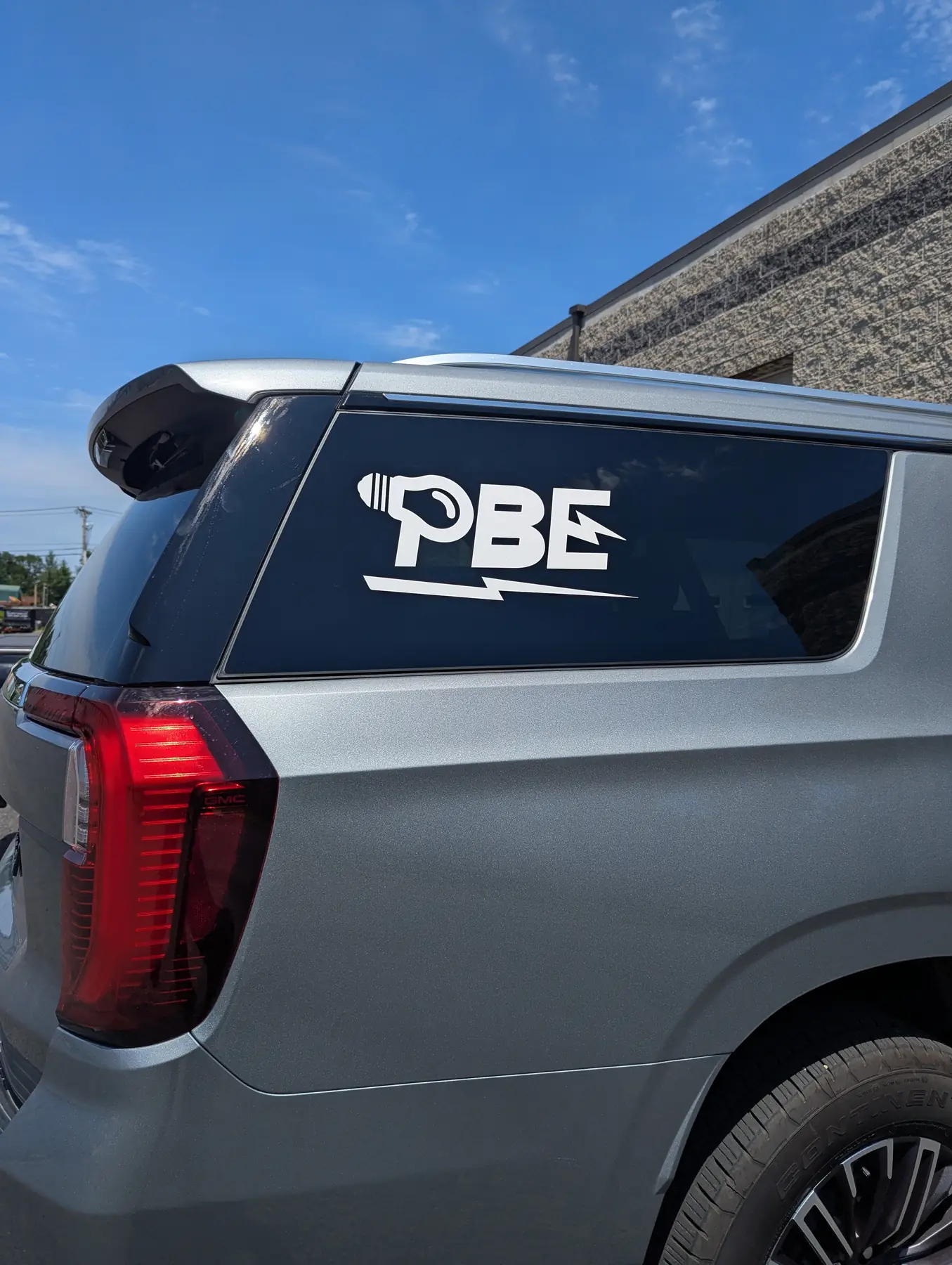 White PBE logo applied to the rear side window of a family vehicle